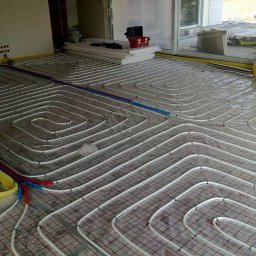 Instalacje sanitarne serwis urządzeń grzewczych - Rozłożone rury ogrzewania podłogowego na siatce, widoczne izolacje brzegowe i materiały budowlane w tle, przygotowanie do wylewki.