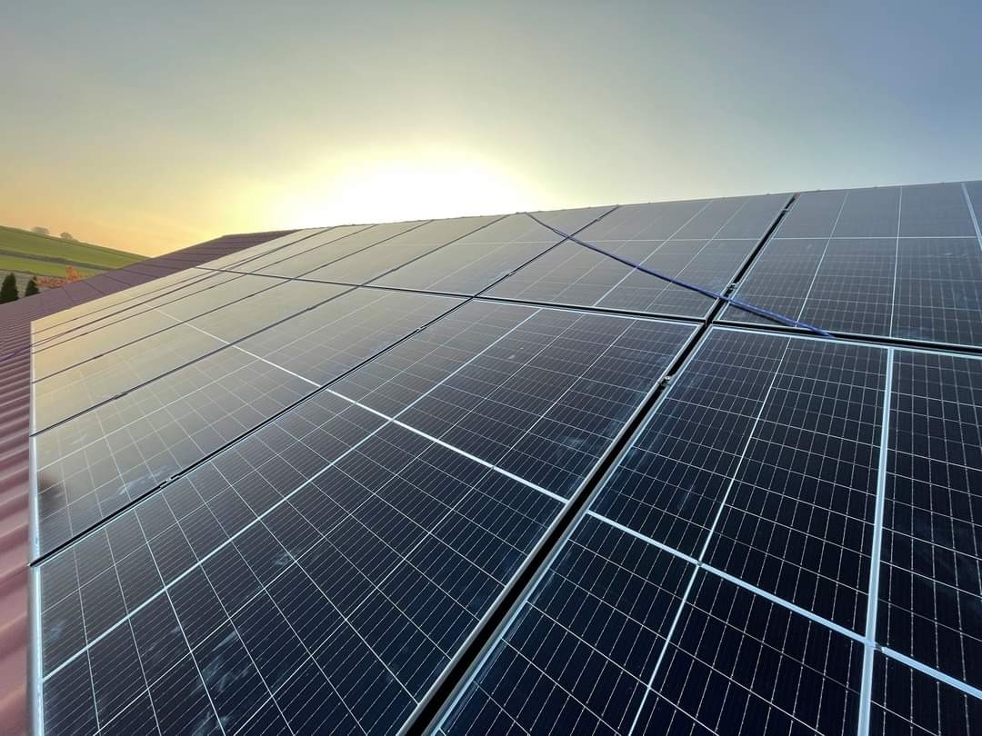 Panele fotowoltaiczne na dachu domu, widok pod kątem, zachodzące słońce odbija się od powierzchni paneli.