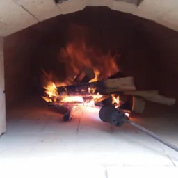 Wnętrze pieca chlebowego z palącym się drewnem i pogrzebaczem, ceglana konstrukcja z widocznymi spoinami.