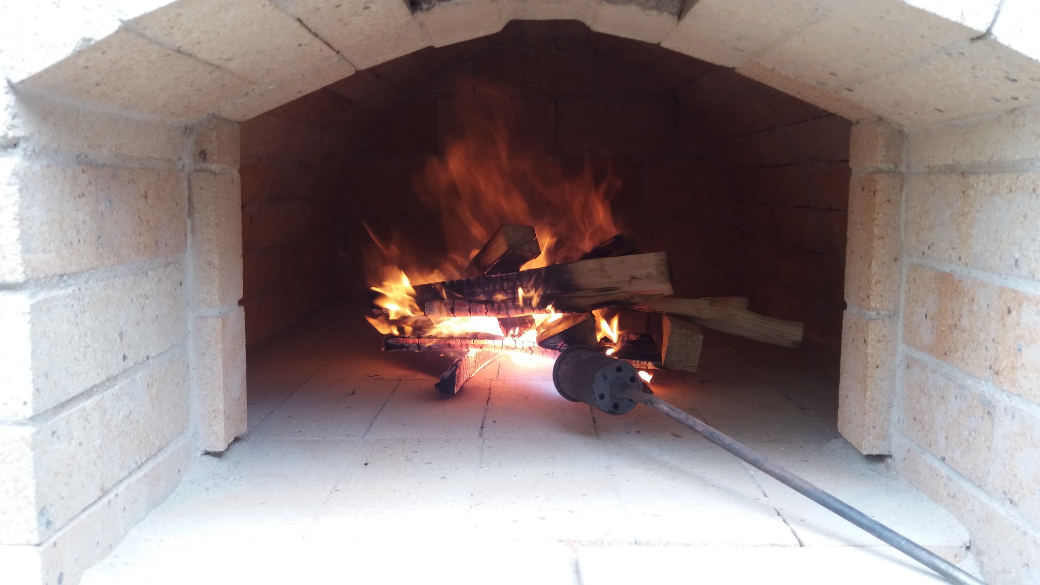 Wnętrze pieca chlebowego z palącym się drewnem i pogrzebaczem, ceglana konstrukcja z widocznymi spoinami.
