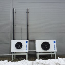 Sigma Chłodnictwo-serwis - Dwa białe agregaty chłodnicze TECHNOb.IT na metalowych podstawach, zamontowane na zewnątrz budynku z szarej blachy trapezowej, widoczne rury instalacyjne i resztki topniejącego śniegu.