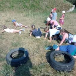 Grupa dzieci na trawie, niektóre czołgają się przez opony, zabawa na świeżym powietrzu, letni dzień.
