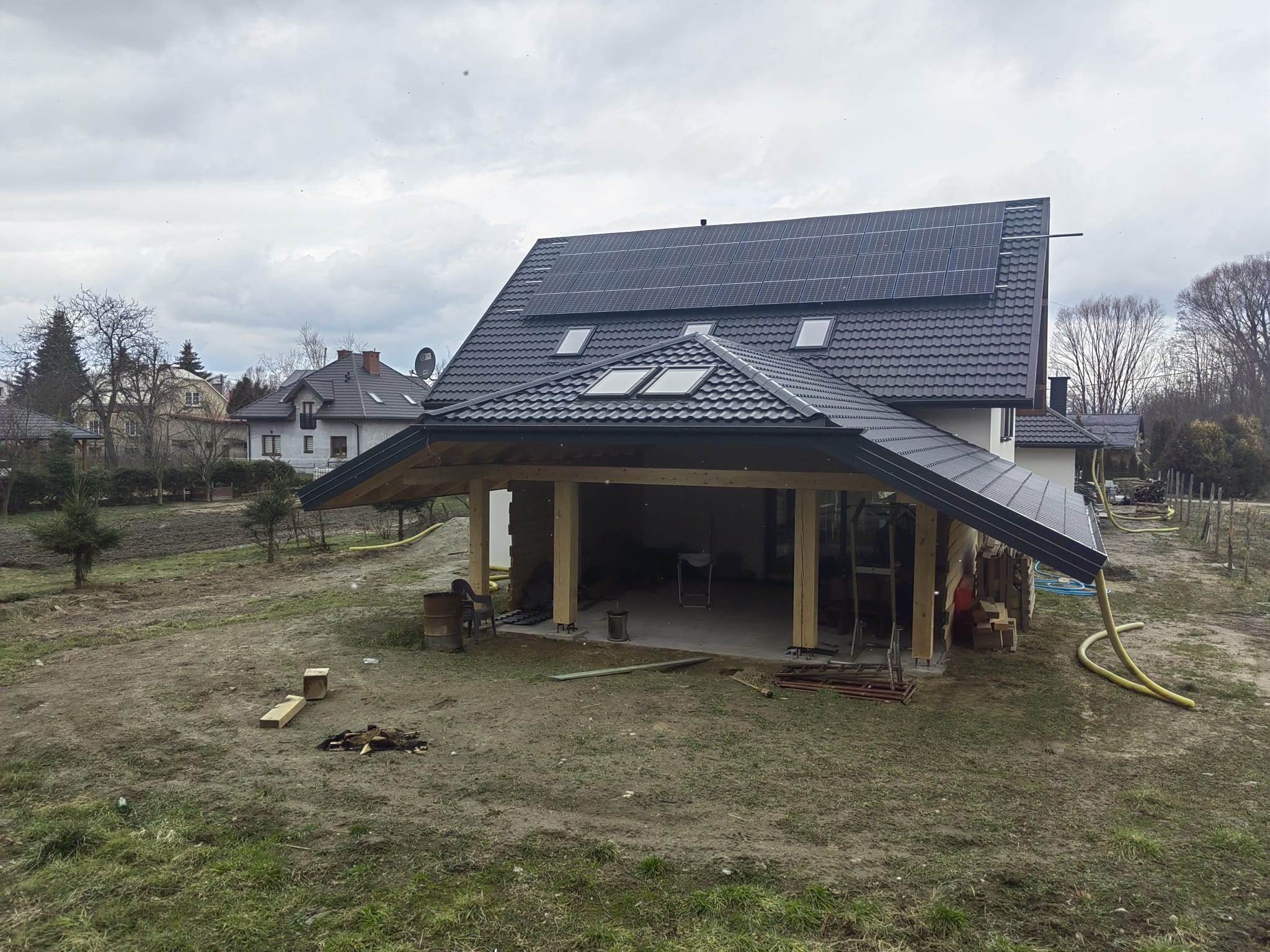 Dom jednorodzinny z nowym dachem z panelami słonecznymi i drewnianą konstrukcją werandy w trakcie budowy, widok z perspektywy ogrodu.