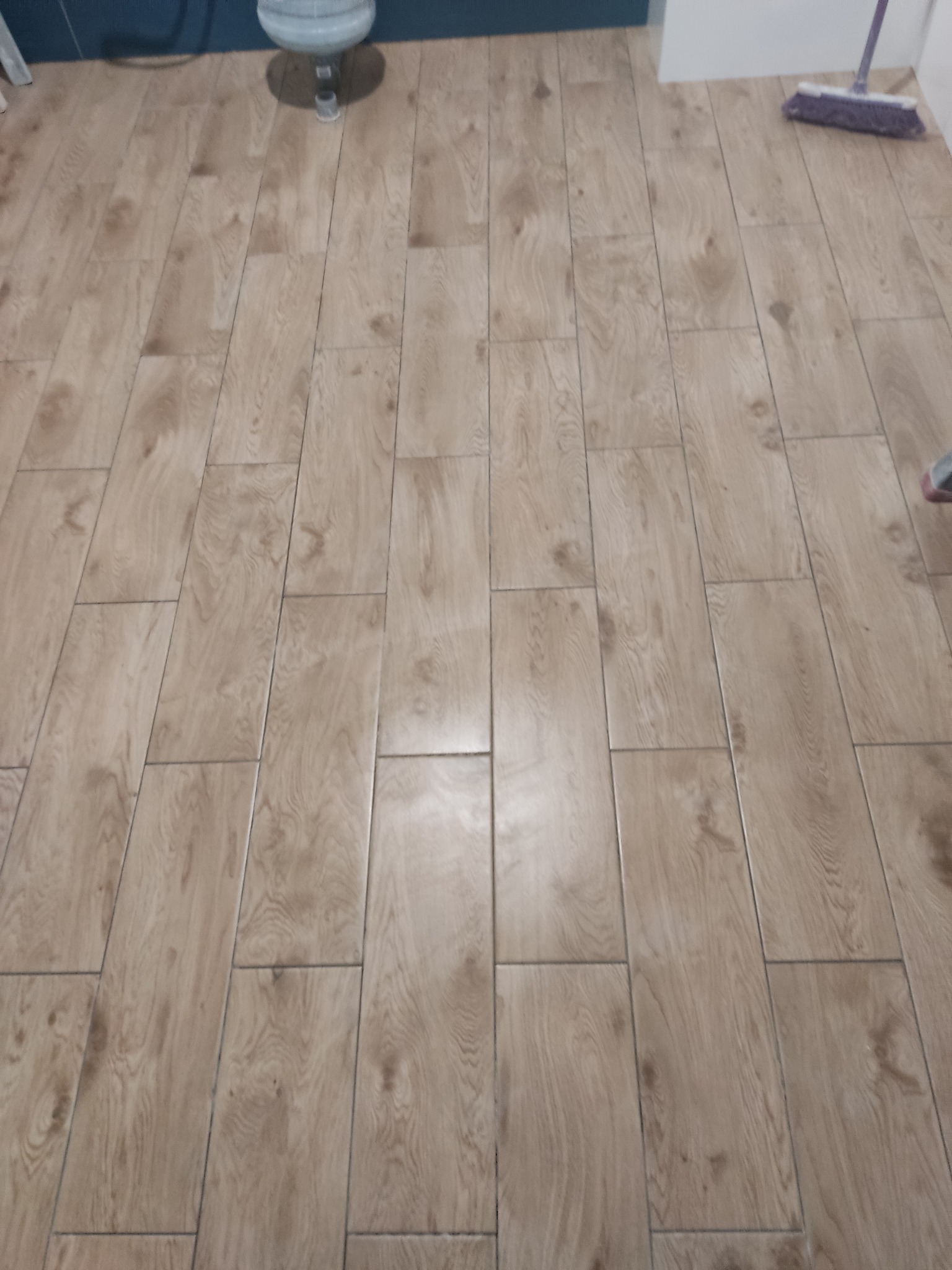 Ułożona podłoga z paneli imitujących drewno w łazience, widoczny fragment toalety i mop.