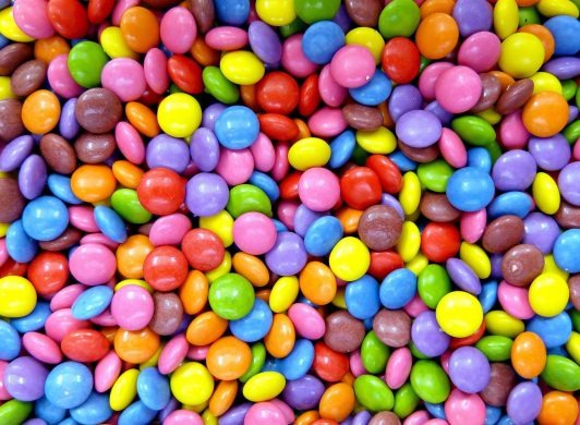 Mnóstwo kolorowych, drażowanych cukierków w odcieniach różu, czerwieni, żółci, zieleni, brązu, fioletu i błękitu, wypełniających całą przestrzeń kadru.