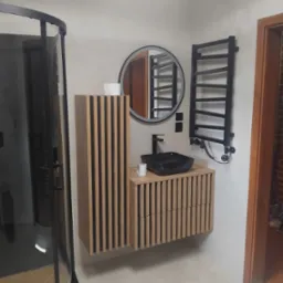 Nowoczesna łazienka z czarną armaturą i drewnianymi lamelami na szafce umywalkowej oraz grzejniku. Kabina prysznicowa z czarnymi profilami.