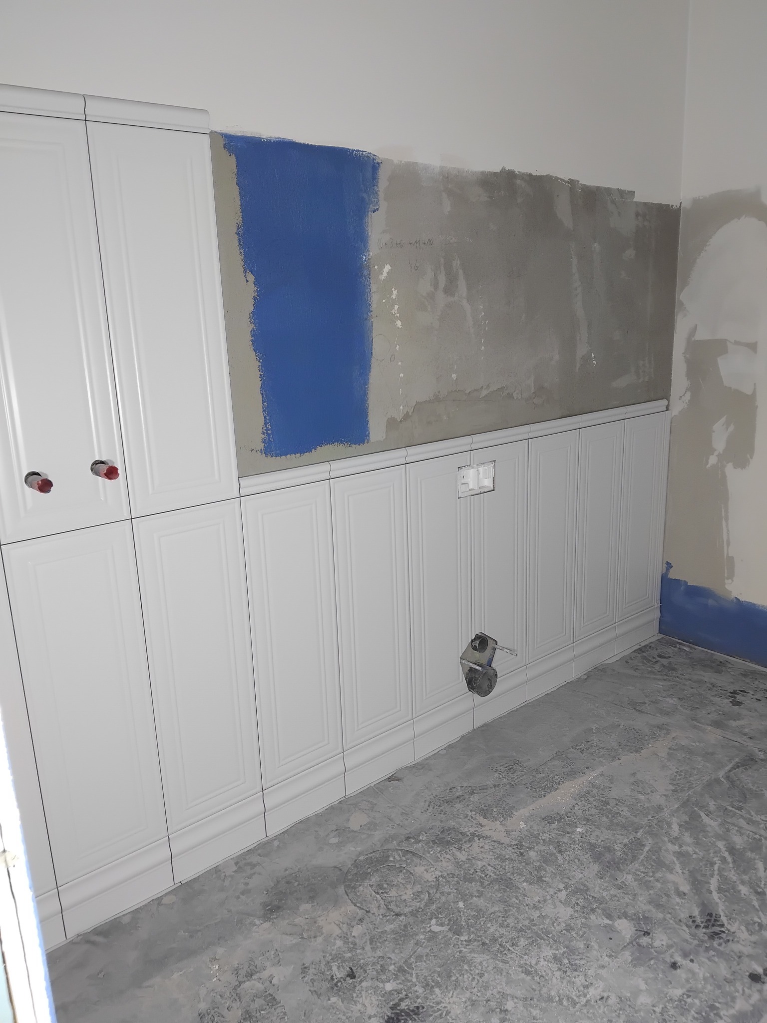 Białe panele ścienne z frezami w trakcie montażu w Połczynie-Zdroju. Fragment ściany z niebieską farbą i instalacją elektryczną. Surowa podłoga.