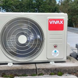 ClimaKor Bartłomiej Kordyk - Zamontowana, beżowa jednostka zewnętrzna klimatyzacji Vivax na betonowej podstawie, z widocznym wentylatorem i logo firmy, na tle zielonych drzew.