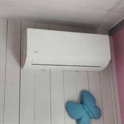 ClimaKor Bartłomiej Kordyk - Biała klimatyzacja Vivax na ścianie z białych paneli, obok różowej ściany z karniszem i ozdobnym, błękitnym motylem poniżej.