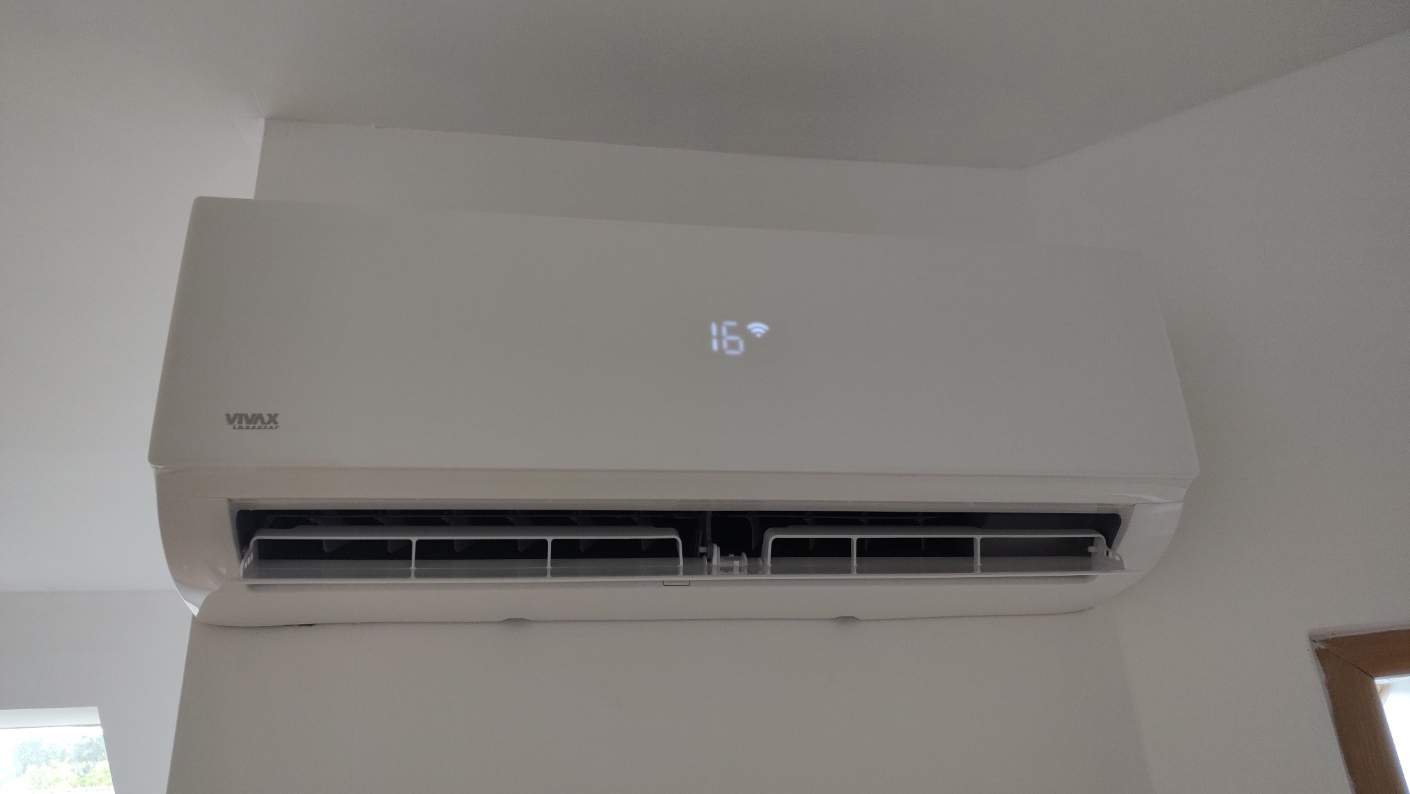 Biała jednostka klimatyzacji VIVAX zamontowana na ścianie, wyświetlająca temperaturę 16 stopni Celsjusza i symbol Wi-Fi.