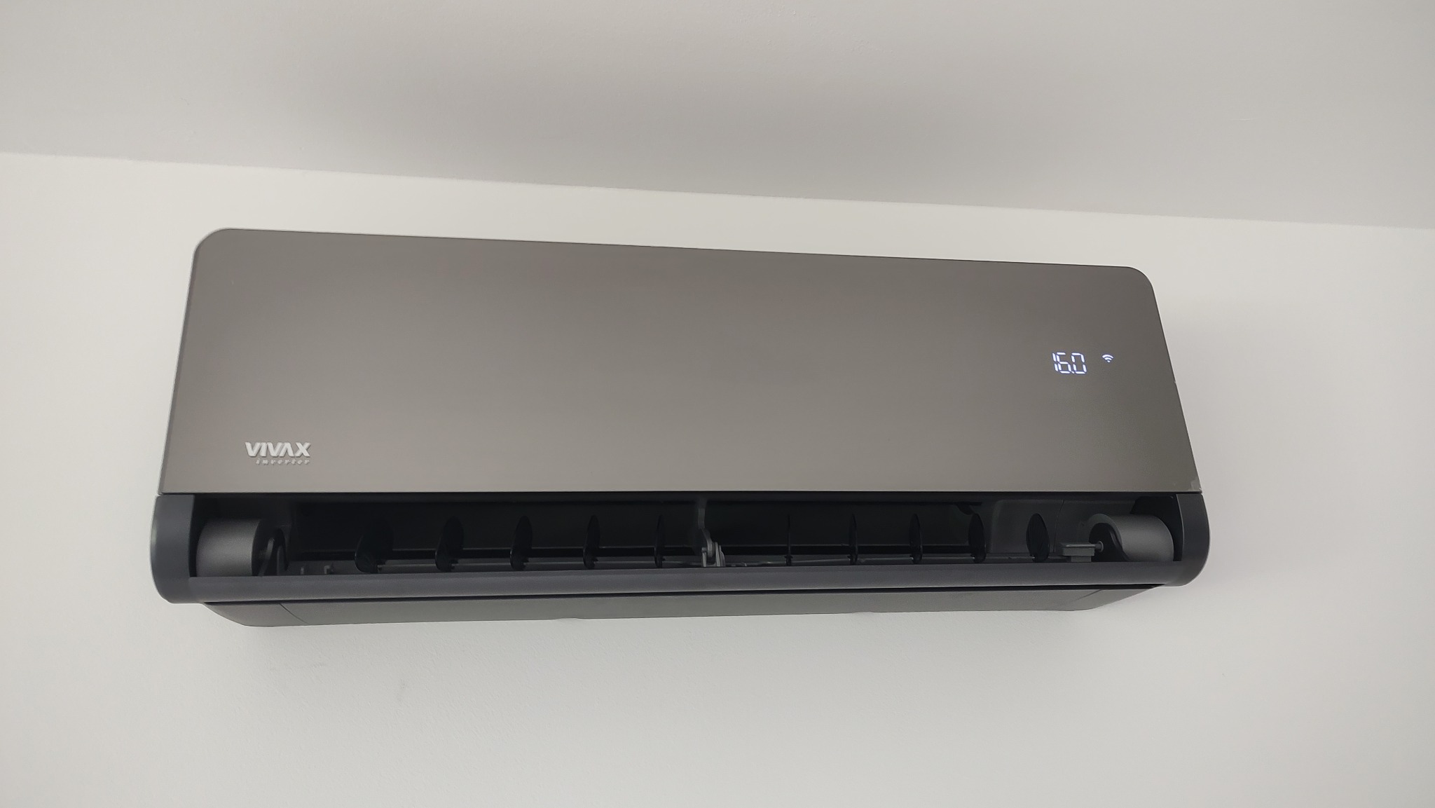 Szary klimatyzator marki Vivax z wyświetlaczem temperatury 16 stopni Celsjusza, zamontowany na białej ścianie.