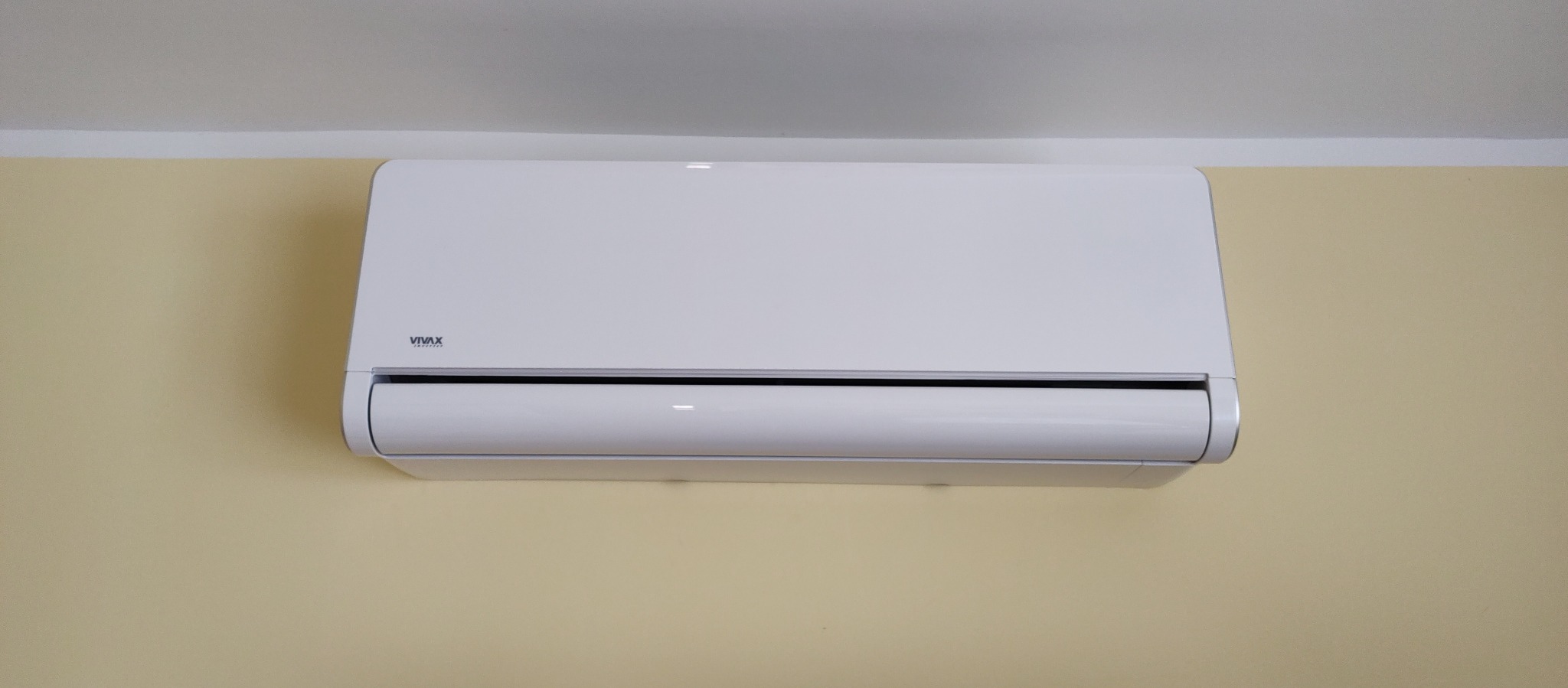 Biały klimatyzator marki Vivax zamontowany na beżowej ścianie w pomieszczeniu.