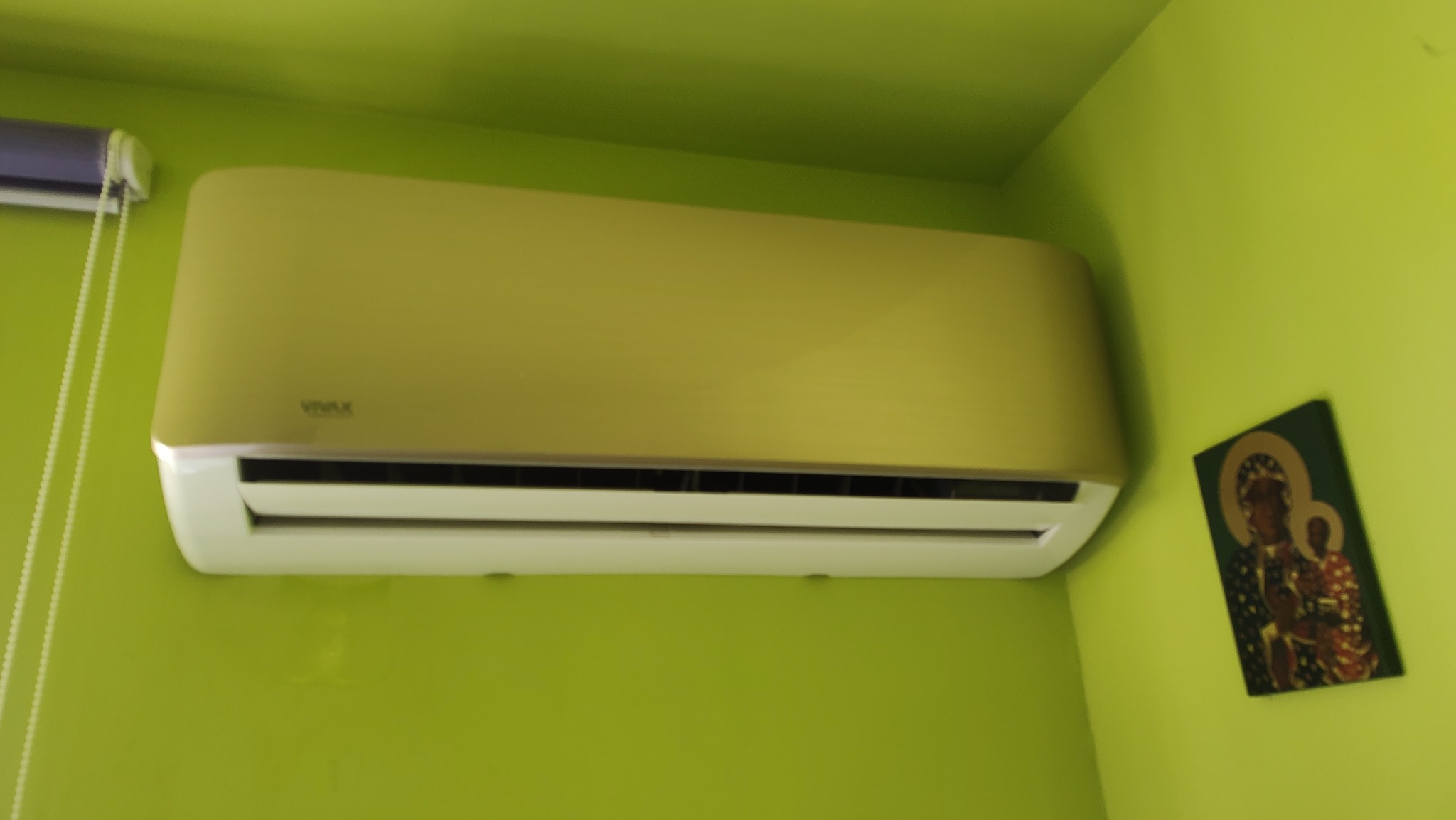 Klimatyzator Vivax zamontowany na jasnozielonej ścianie, obok ikony religijnej.