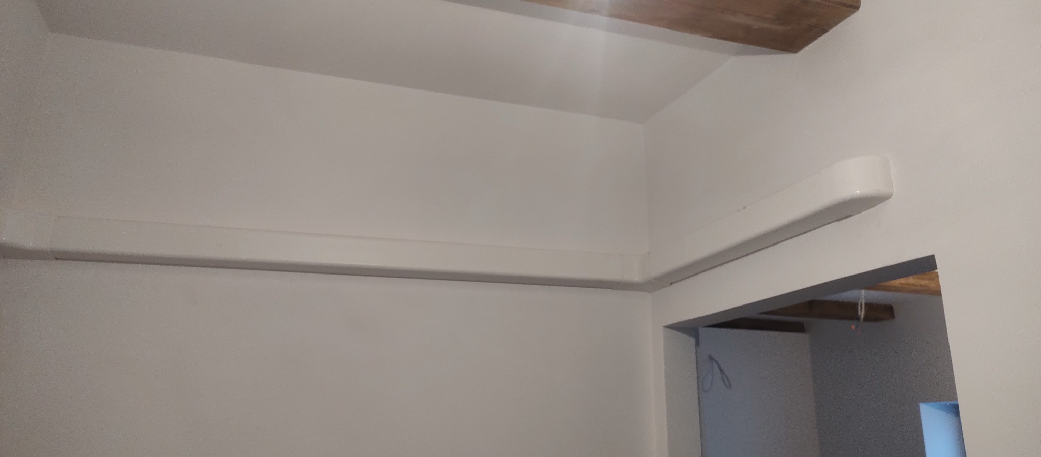 Biała listwa maskująca instalację klimatyzacyjną, zamontowana pod sufitem w rogu pomieszczenia, widoczna z perspektywy narożnika pokoju.