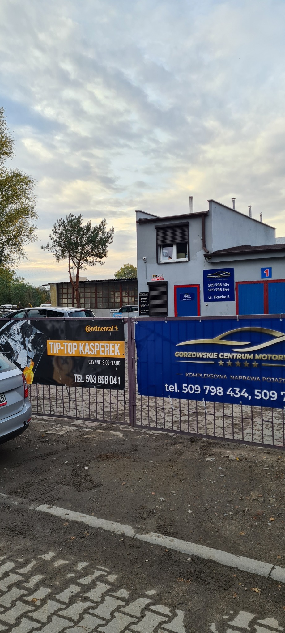 Budynek warsztatu samochodowego z reklamowymi banerami firm 'Tip-Top Kasperek' i 'Gorzowskie Centrum Motory', widok z zewnątrz, pochmurne niebo.