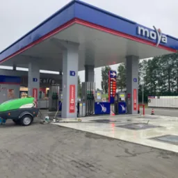 Stacja paliw Moya: świeżo umyta kostka brukowa na podjeździe, widoczny zielony wózek z urządzeniem do czyszczenia pod ciśnieniem i mokre plamy po myciu.