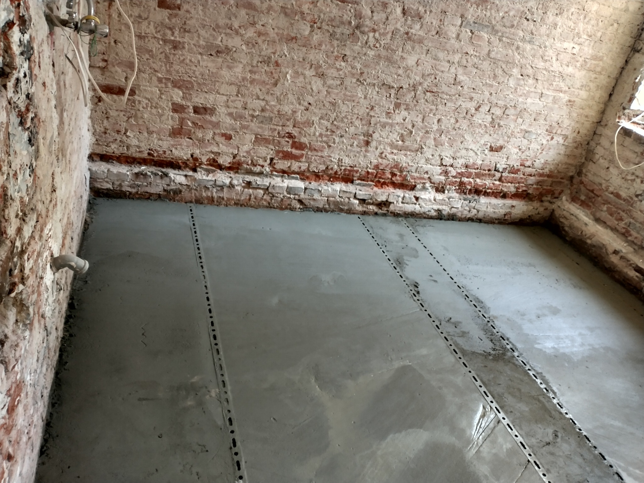 Wylewka samopoziomująca z listwami dylatacyjnymi na nierównej, ceglanej podłodze w trakcie remontu.