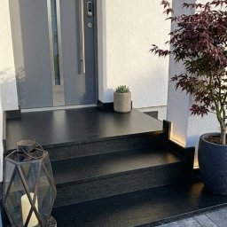 Płytki Max - Nowoczesne, czarne schody kamienne prowadzące do domu z numerem 14A, oświetlone subtelnym światłem LED, z dekoracyjną latarnią i roślinami w donicach.