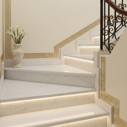 Płytki Max - Eleganckie, marmurowe schody z podświetleniem LED i dekoracyjnym motywem greckim na ścianach. Wazon z białymi kwiatami na podeście.