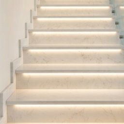 Płytki Max - Marmurowe schody z podświetleniem LED, szklana balustrada, dekoracyjny wazon na górnym stopniu. Nowoczesny design, jasne wnętrze, eleganckie wykończenie.