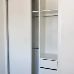 Biała szafa przesuwna z trzema szufladami i drążkami na ubrania, minimalistyczny design, jasne wnętrze, widoczne detale systemu przesuwnego.