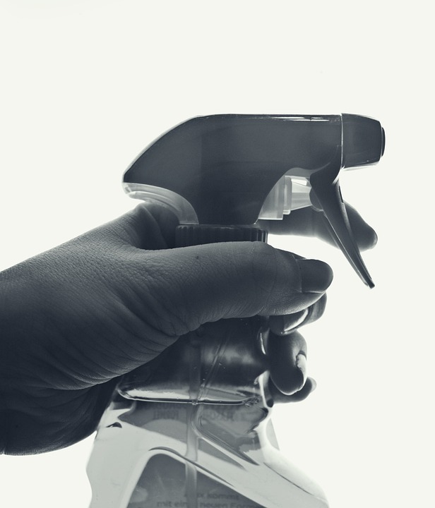 Dłoń trzymająca spryskiwacz z płynem, przygotowany do użycia, na białym tle.