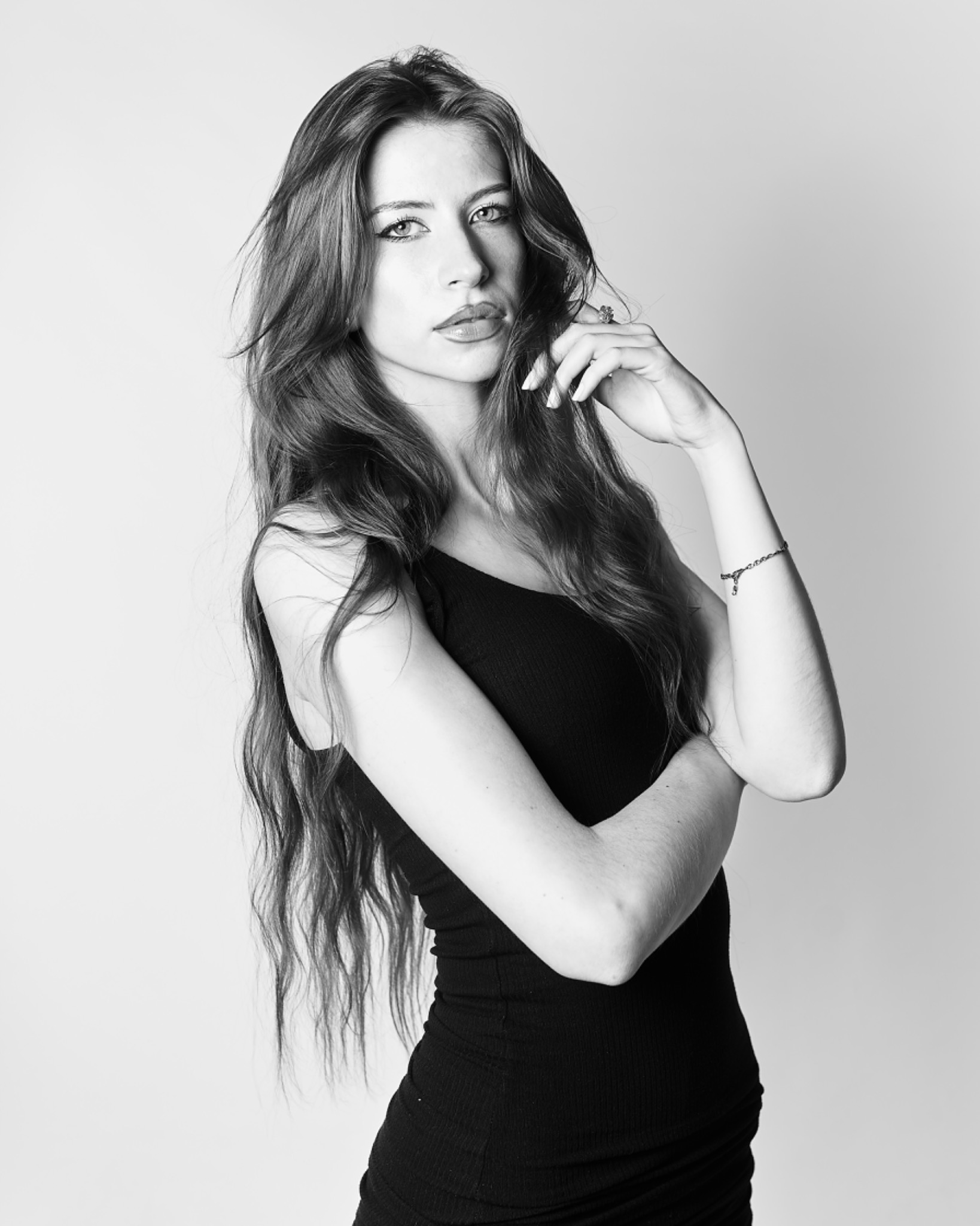 Portret kobiety w czarnej sukience, z długimi włosami i delikatną biżuterią, wykonany w czerni i bieli.