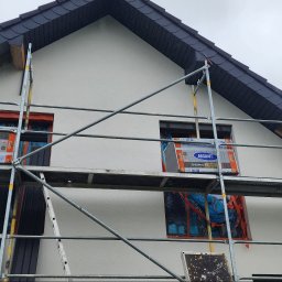 Morozov BUD - Dom jednorodzinny w trakcie prac elewacyjnych, zabezpieczone okna, widoczne rusztowania i opakowanie styropianu termoizolacyjnego Arsanit.