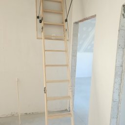 Morozov BUD - Drewniane schody strychowe rozłożone w surowym wnętrzu, widoczne niedokończone ściany i instalacje. Kąt ujęcia od dołu, ukazujący mechanizm składania.