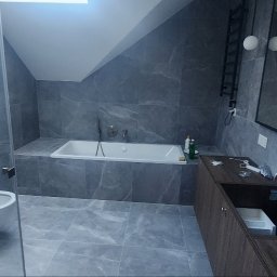 Morozov BUD - Wykończona łazienka na poddaszu we Wrocławiu z szarymi płytkami imitującymi marmur, białą wanną i wiszącą toaletą. Nowoczesny styl.