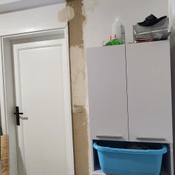 Morozov BUD - Remont łazienki: wyrównywanie ścian gipsem przy drzwiach i szafce. Widoczne narzędzia, wzorzysta podłoga. Etap prac wykończeniowych w pomieszczeniu.