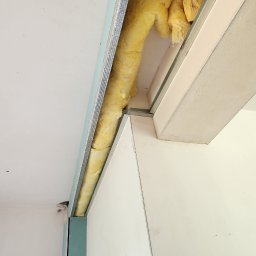 Morozov BUD - Ocieplenie wełną mineralną w szczelinie sufitu podwieszanego, widoczne profile konstrukcyjne i płyta gipsowo-kartonowa. Ujęcie z dołu, z bliska.