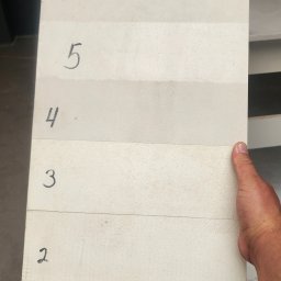 Morozov BUD - Próbka elewacji z numerami od 1 do 6, ukazująca różne tekstury i odcienie bieli. Widoczna siatka wzmacniająca na próbce nr 1. Ręka trzyma próbkę.