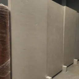 Wykończone ściany w odcieniach beżu, wsparte na białych bloczkach. Widoczna faktura tynku i fragment zabezpieczonego folią materiału budowlanego.