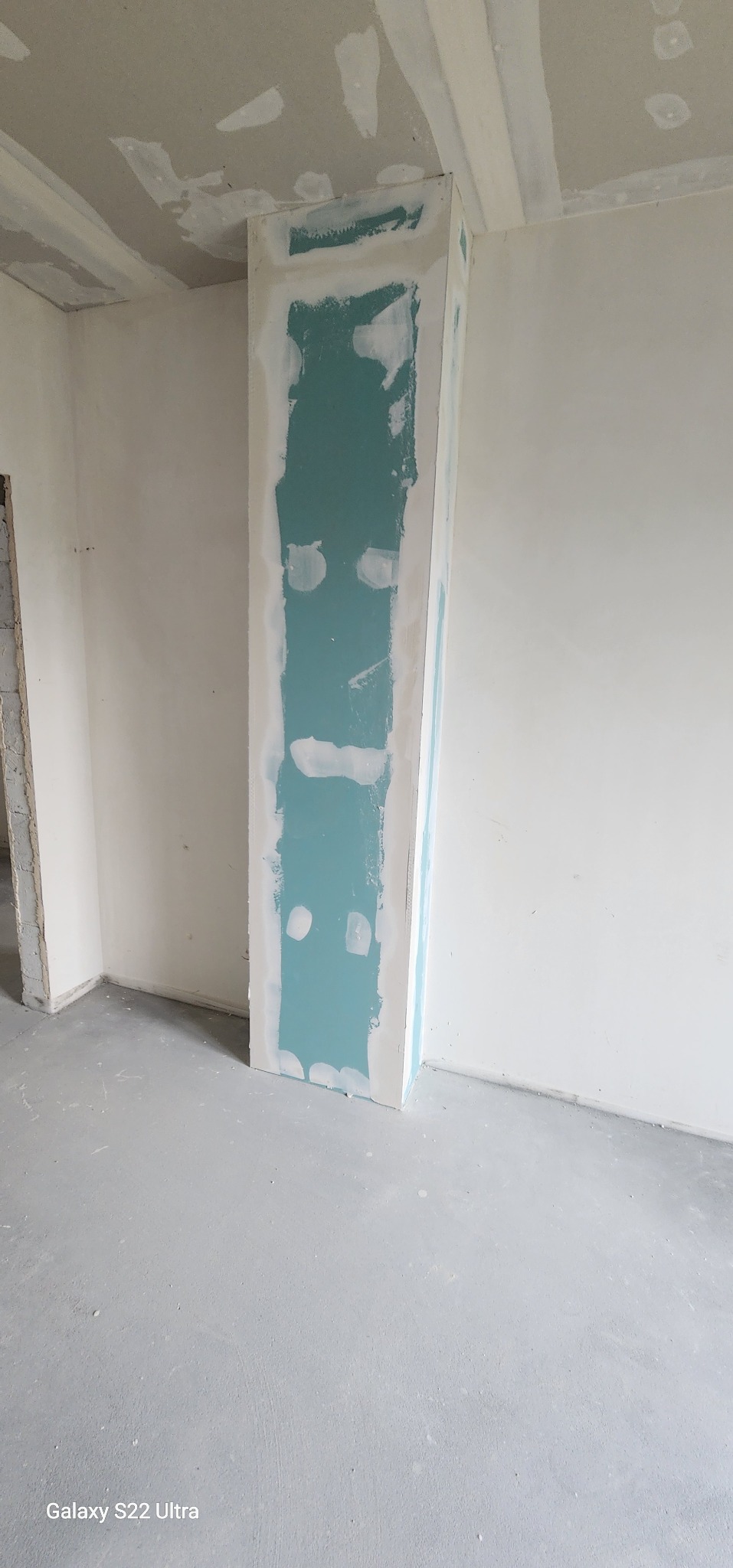 Pionowa konstrukcja z płyty gipsowo-kartonowej, wstępnie wykończona szpachlą, w narożniku pomieszczenia w trakcie prac wykończeniowych.