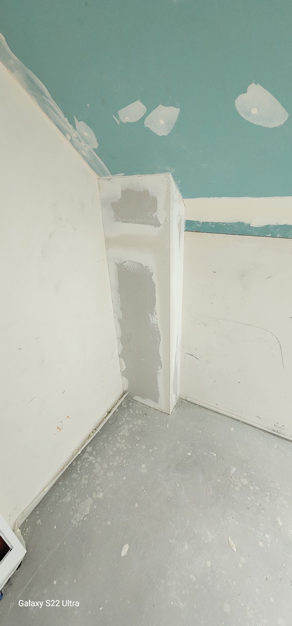 Wnętrze w trakcie prac wykończeniowych: ściany i sufit pokryte gładzią gipsową, widoczne ślady po szpachlowaniu. Narożnik zabezpieczony profilem.