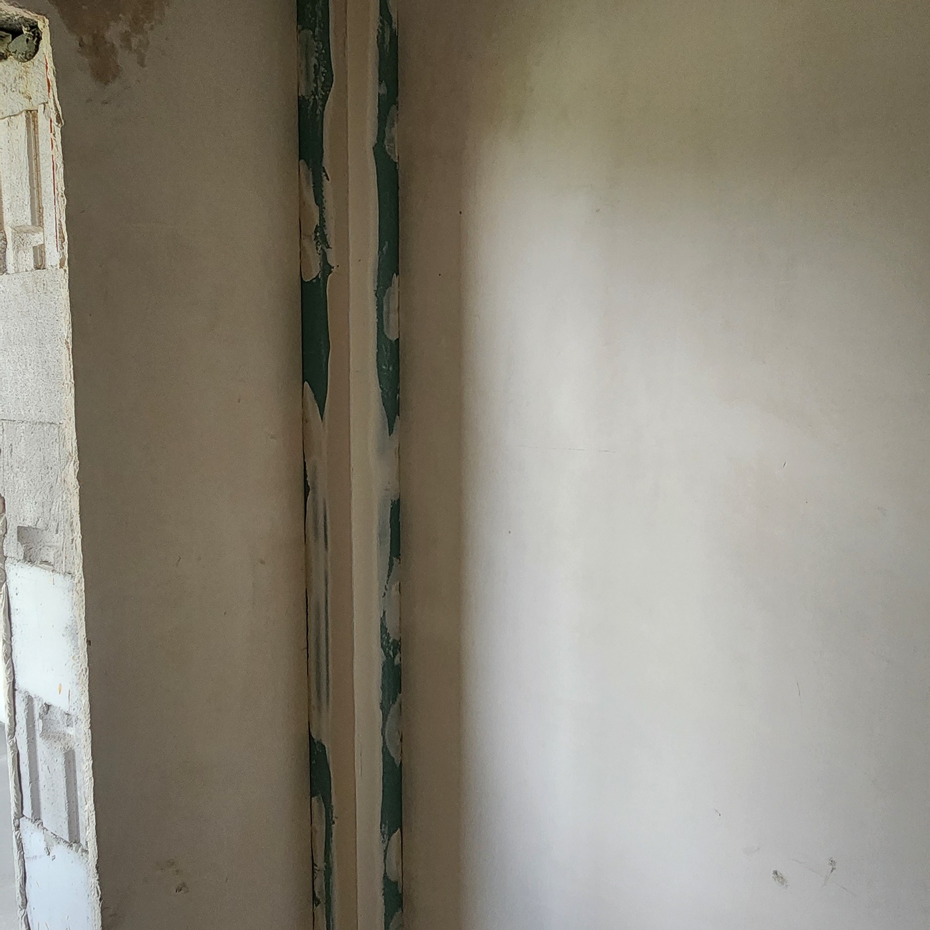 Ściana w trakcie remontu, widoczne pionowe rury zabezpieczone taśmą malarską, surowa ściana z pustaków po lewej stronie, przygotowania do dalszych prac wykończeniowych.