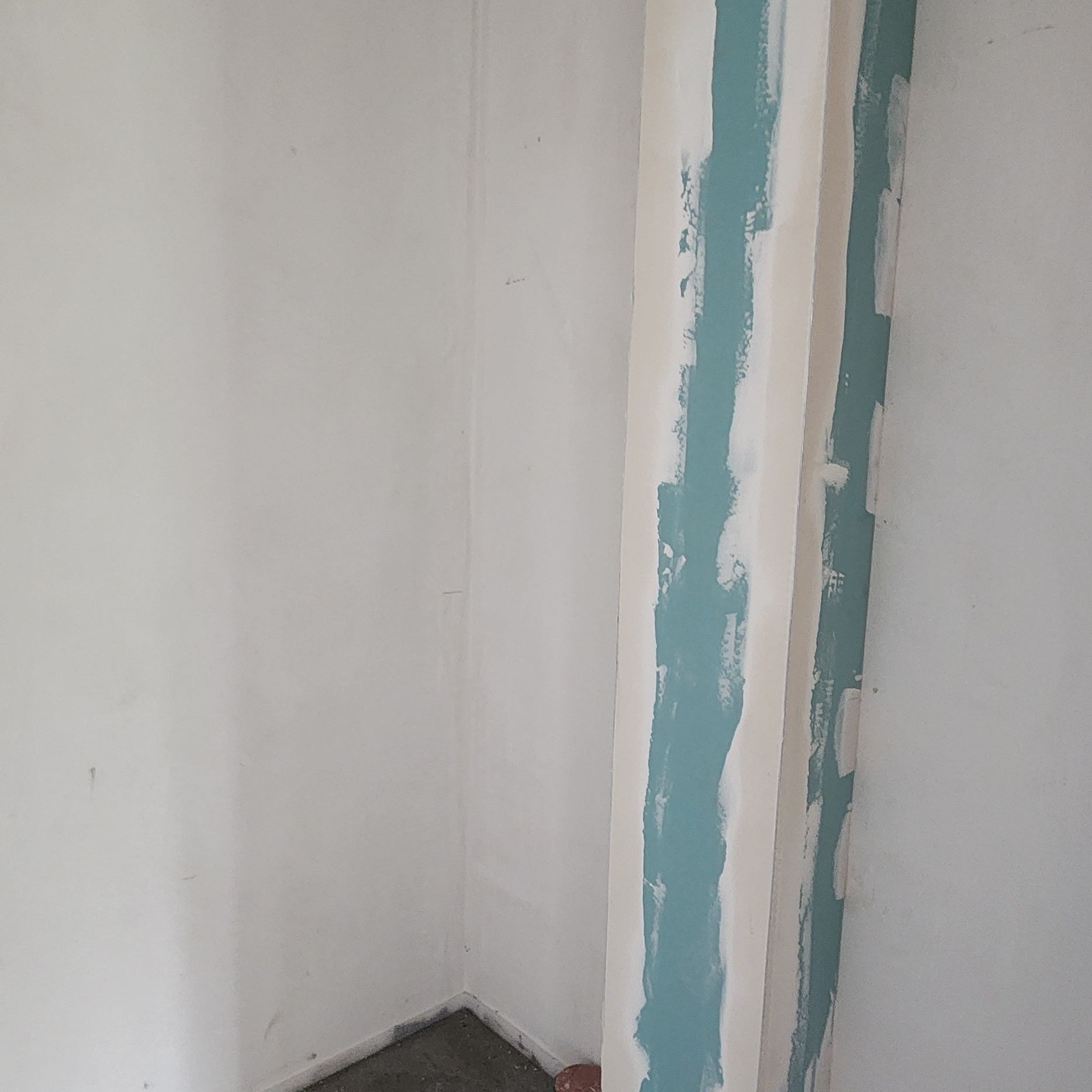 Wnętrze w trakcie prac wykończeniowych: ściana z nałożoną gładzią gipsową na narożniku, przygotowana do malowania. Widoczne ślady szpachlowania.