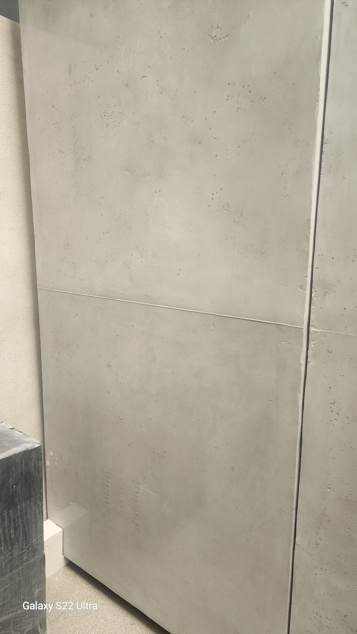 Szare, betonowe płyty ścienne z widoczną fugą, ułożone w poziomie. Delikatna tekstura betonu z drobnymi porami. Minimalistyczny design, nowoczesne wykończenie wnętrza.