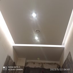 ZAG-BUD USŁUGI WYKOŃCZENIOWE i BUDOWLANE - Nowoczesny sufit podwieszany z oświetleniem LED w trakcie montażu, widoczne niedokończone ściany i otwór wentylacyjny.