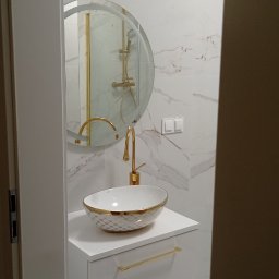 ZAG-BUD USŁUGI WYKOŃCZENIOWE i BUDOWLANE - Nowoczesna łazienka z umywalką nablatową w geometryczny wzór z złotymi akcentami, złotą armaturą i okrągłym lustrem z podświetleniem, marmurowe płytki na ścianach, minimalistyczny design.