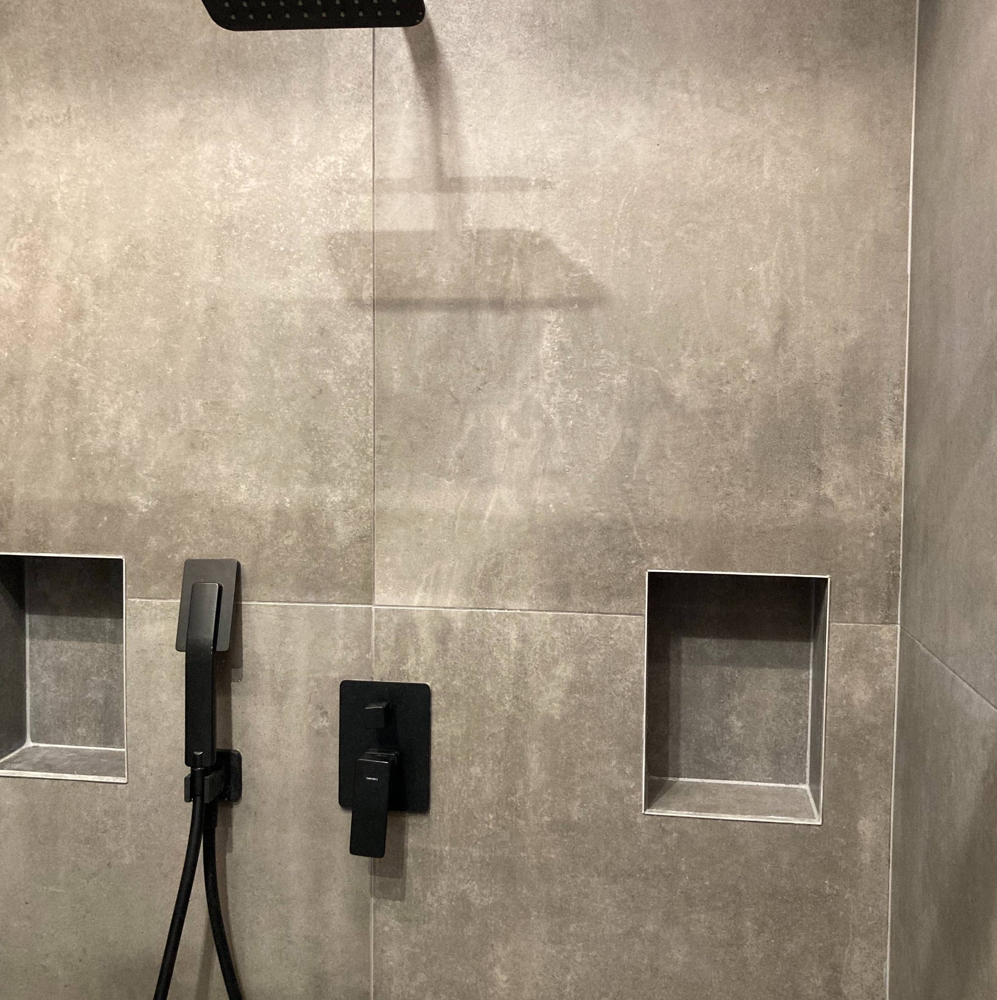 Szare płytki w kabinie prysznicowej z czarną armaturą i wnękami ściennymi.