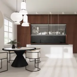 Jasne, minimalistyczne wnętrze jadalni z okrągłym stołem na czarnej podstawie, krzesłami z jasną tapicerką i otwartą kuchnią z drewnianymi szafkami w tle. Nad stołem wiszą nowoczesne, białe lampy.