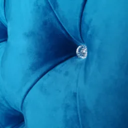 Fragment pikowanego zagłówka łóżka obitego turkusowym welurem, ozdobionego kryształowym guzikiem.