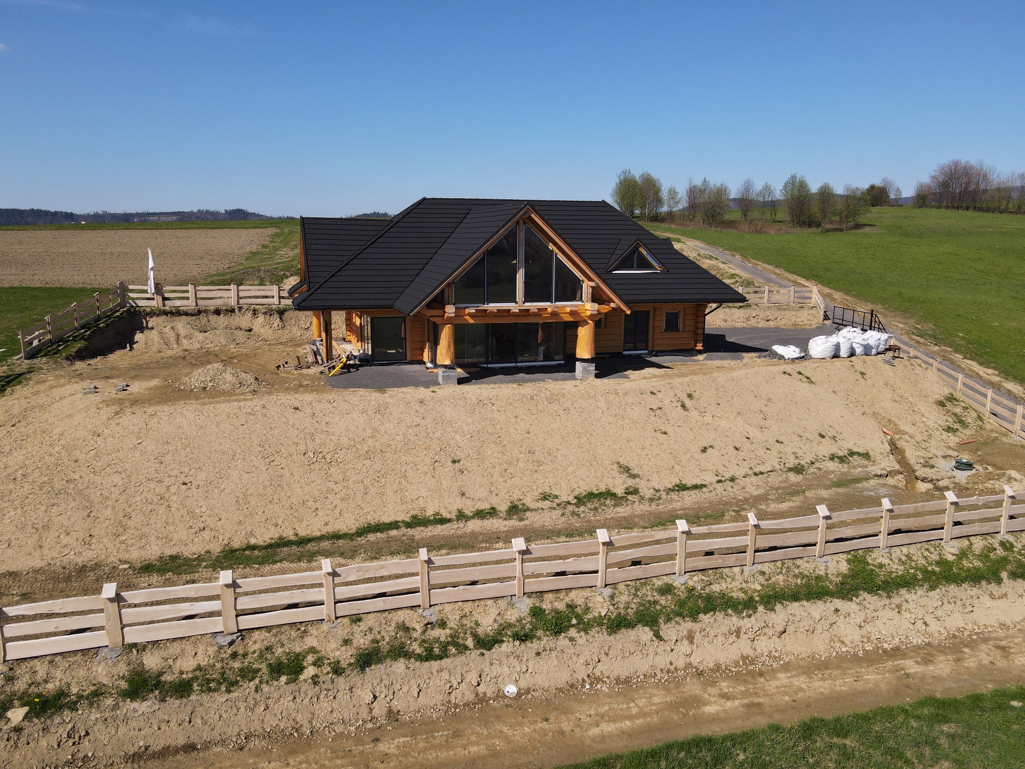 Nowoczesny dom z bali z czarnym dachem, dużymi oknami i drewnianym ogrodzeniem na wzgórzu, widok z góry.