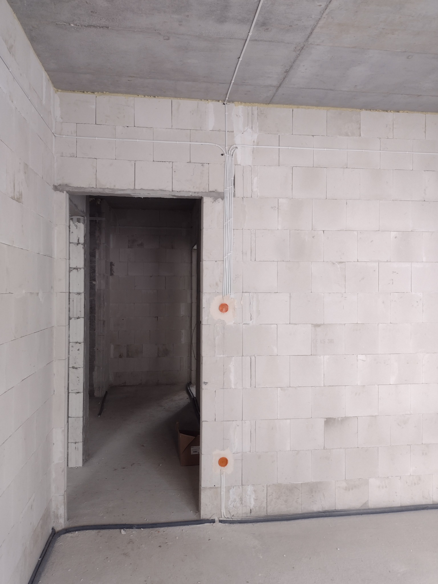 Wewnętrzne ściany z betonu komórkowego w stanie surowym z widocznymi przewodami elektrycznymi w peszlach i puszkami instalacyjnymi, przed tynkowaniem.