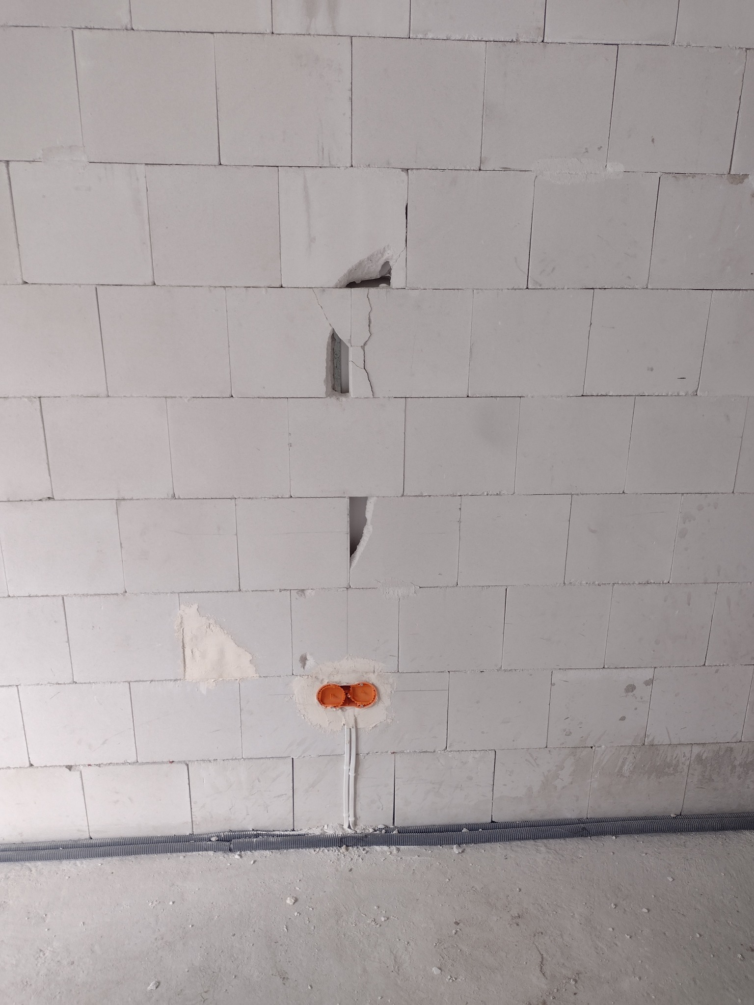 Ściana z betonu komórkowego z wyciętymi otworami na puszki elektryczne i bruzdami na przewody, widoczne peszle przy podłodze.