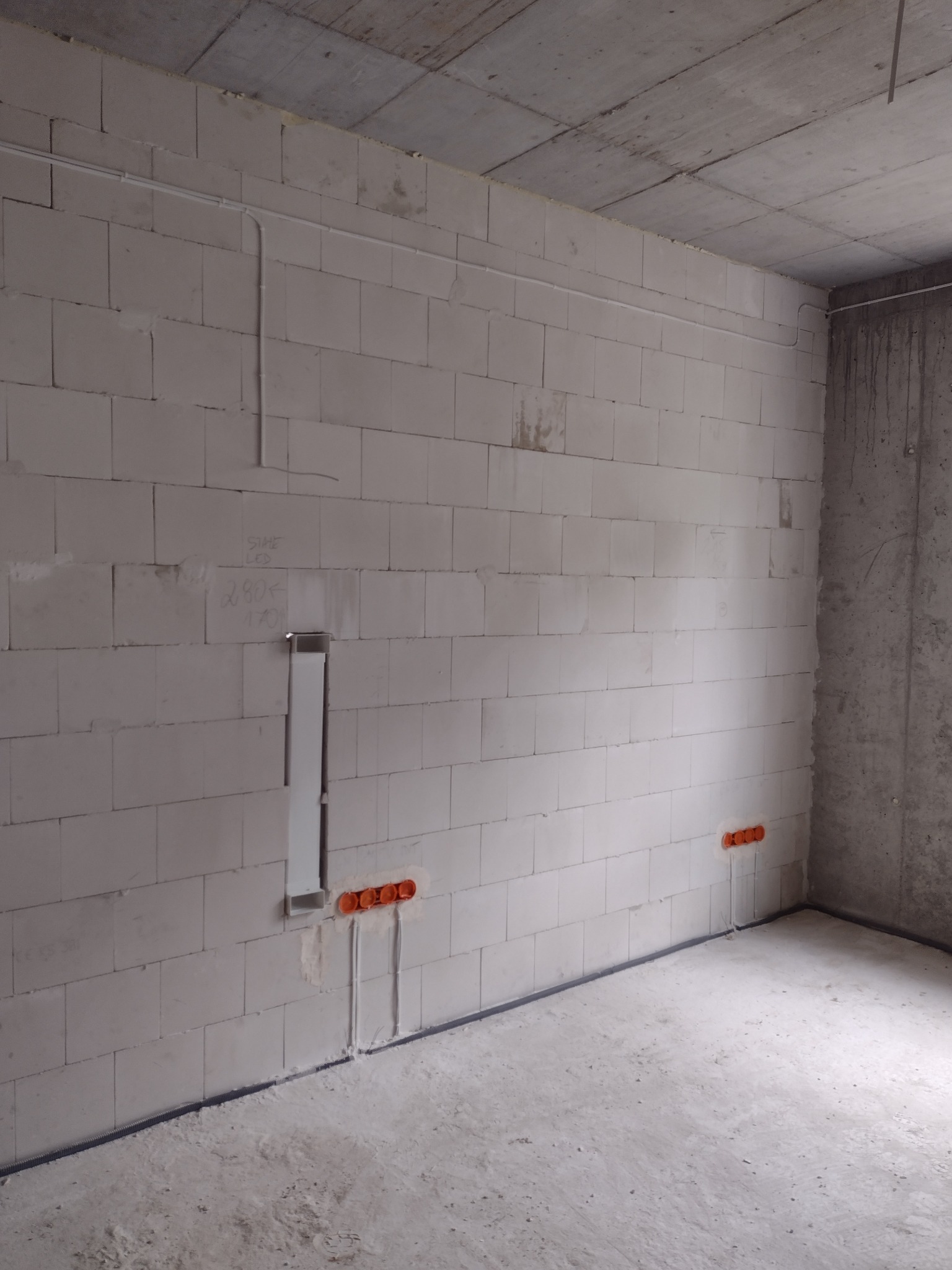Surowy stan wnętrza z widocznymi przewodami i puszkami elektrycznymi w ścianie z betonu komórkowego, oraz rurkami PCV przy podłodze, przygotowanymi do dalszych prac.