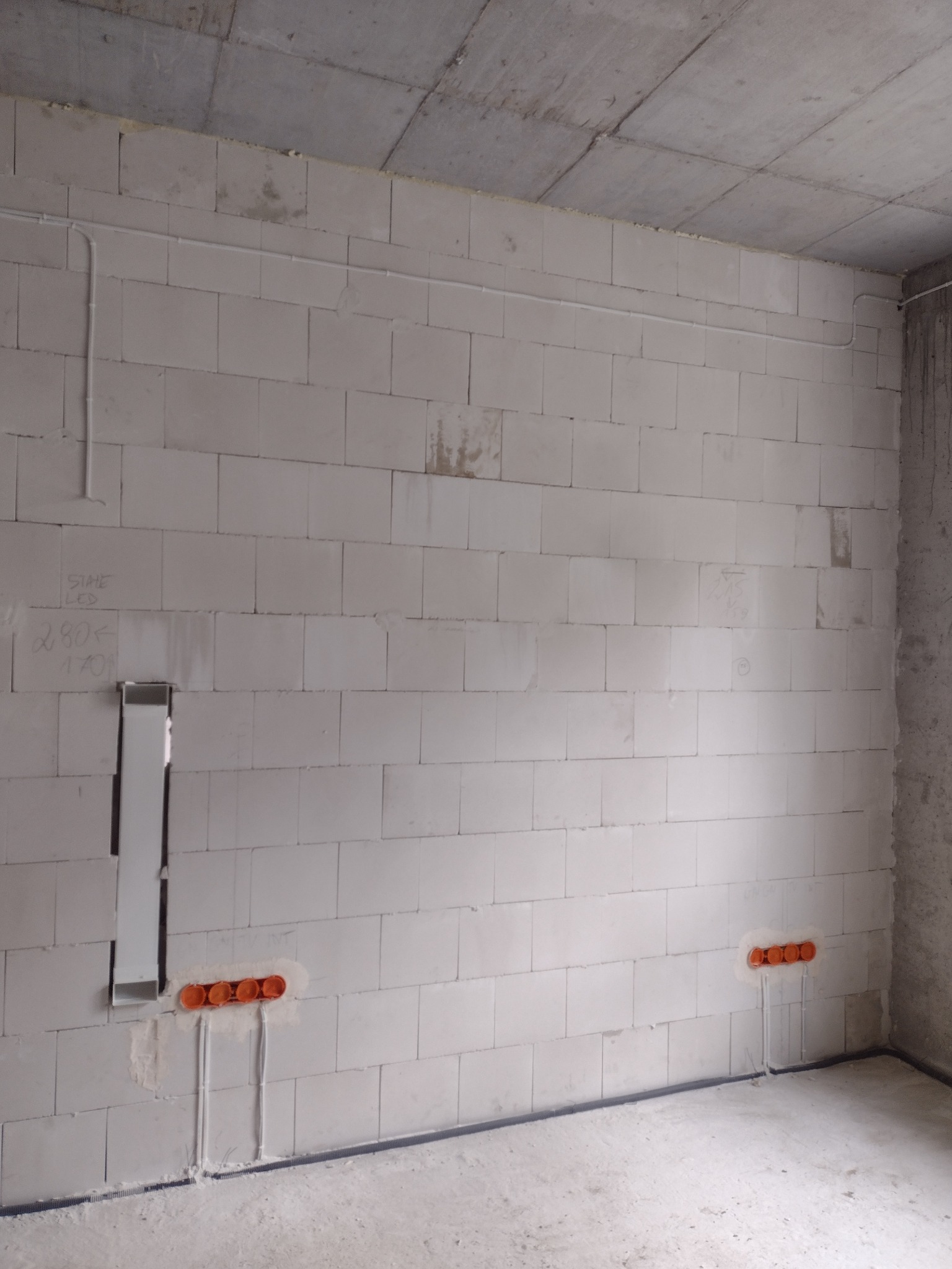 Surowa ściana z betonu komórkowego z widocznymi puszkami elektrycznymi i przewodami, w trakcie instalacji elektrycznej.