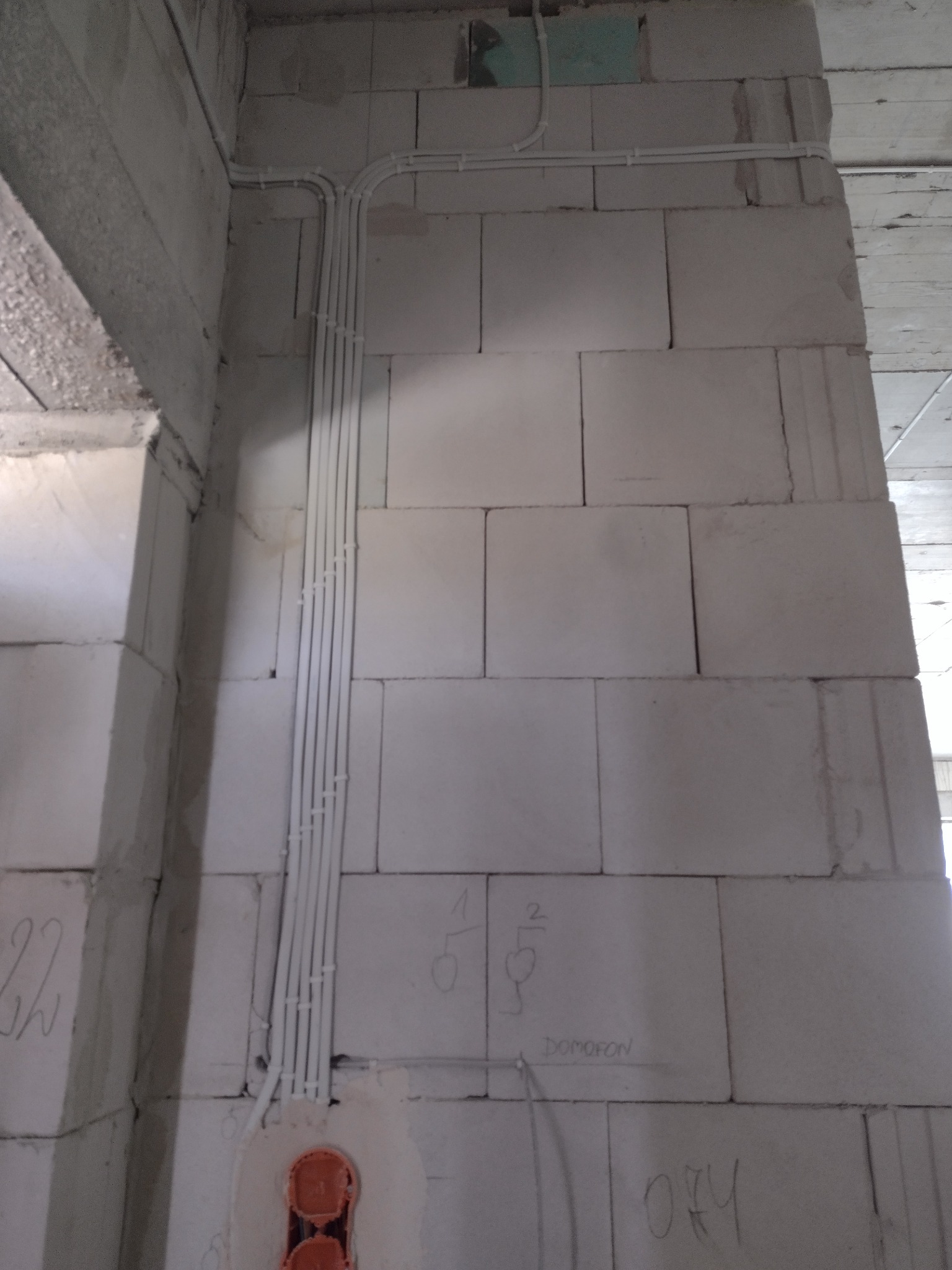 Ściana z betonu komórkowego w trakcie instalacji elektrycznej: peszle z przewodami ułożone pionowo, puszka instalacyjna podwójna, oznaczenia ołówkiem na ścianie.